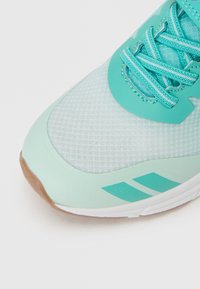 Τυρκουάζ αθλητικό παπούτσι με επάνω μέρος από δίχτυ, υφασμένο δάχτυλο και πλεκτά κορδόνια. Διαθέτει τρεις διαγώνιες ρίγες σε πιο ανοιχτή απόχρωση και λαστιχένια σόλα.