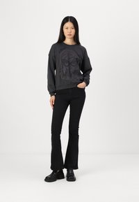Felpa nera con una grafica del volto di una donna, abbinata a jeans neri a zampa d'elefante e scarpe nere chunky. Texture liscia e vestibilità casual.