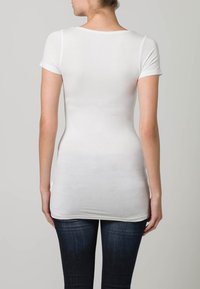 Bijela uska majica s kratkim rukavima, glatke tkanine i okruglim izrezom, u kombinaciji s tamnoplavim trapericama.