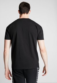 Černé bavlněné tričko, krátké rukávy, design s kulatým výstřihem a hladkou texturou. Viditelné švy na ramenou a na zádech.