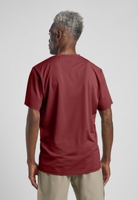 Bordeauxkleurig T-shirt met korte mouwen, gemaakt van ademende stof. Eenvoudige ronde halslijn, zachte textuur en een relaxte pasvorm. De achterkant heeft geen logo's.