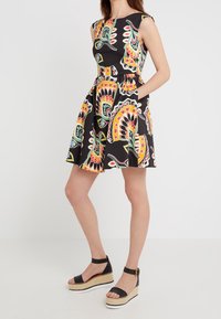 Musta hihaton mekko, jossa on värikäs paisley-kuvio, laakea hame ja sivutaskut. Yhdistettynä mustiin koronkeihin sandaaleihin.