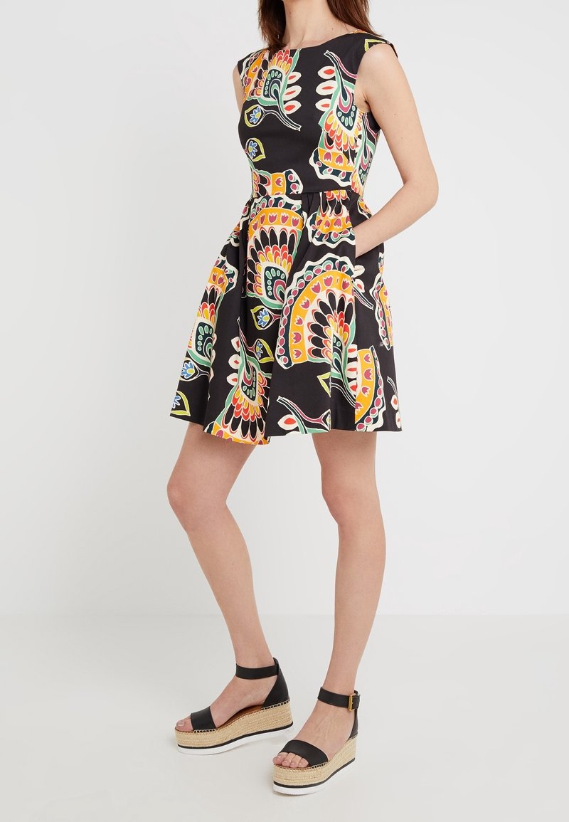 Musta hihaton mekko, jossa on värikäs paisley-kuvio, laakea hame ja sivutaskut. Yhdistettynä mustiin koronkeihin sandaaleihin.