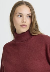 Burgundy színű, garbós pulóver ribbelt nyakkivágással, puha tapintással és laza szabással, hosszú ujjal, látható minták nélkül.