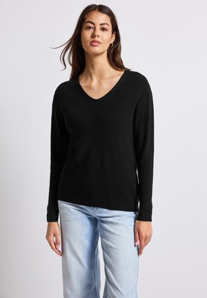 Suéter negro de manga larga con un diseño de escote en V, textura acanalada y un corte relajado. Combinado con jeans de color azul claro.