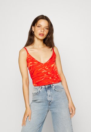 Top vermelho sem mangas com um decote V raso, apresentando um padrão texturizado subtil. Combinado com jeans de cintura alta azul claro.