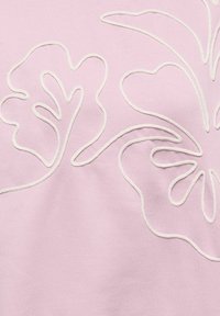 Un tissu rose clair présente des motifs floraux brodés en blanc, avec des lignes fluides et des formes curvilignes, créant un aspect texturé et en couches.