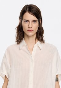 White, short-sleeve button-up shirt in lightweight, textured fabric with a grid pattern and a classic collar. Features a relaxed fit.