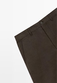 Ceinture de pantalons marron foncé avec passants pour ceinture, fermeture avant à bouton et poche latérale sur fond blanc.