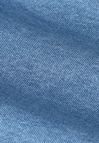 Tissu en denim bleu clair, présentant une texture lisse avec des motifs de tissage visibles. Le matériau semble doux avec de légères variations de teinte.