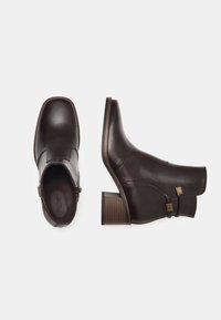 Bottines en cuir marron avec un bout carré, un talon empilé, un accent de boucle sur le côté et une texture lisse. Présente des coutures contrastantes.