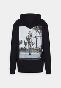 Sudadera con capucha negra que presenta un gran gráfico en la parte de atrás que representa una escena de baloncesto con palmeras y texto en la parte inferior.