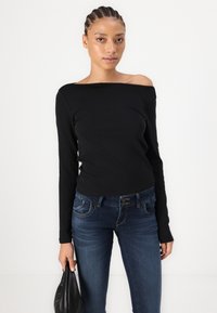 Top nero off-shoulder a maniche lunghe abbinato a jeans slim-fit blu scuro. Il top ha una texture liscia, mentre i jeans presentano cuciture dettagliate.