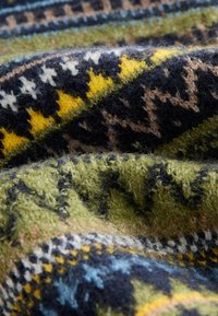 Süvendatud kangas sisaldab geomeetrilisi mustreid tumesinises, rohelises, kollases ja beežis. Tekstuur on pehme ja karvane, näidates keerukaid detaile.