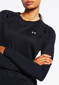 Svart långärmad träningsskjorta med en slät yta, med en ribbad halsringning och en liten vit logotyp på övre vänster sida.