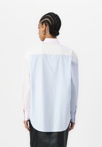 Long-sleeved shirt featuring a mix of light pink and blue stripes, with a white yoke and rounded back hem, made of smooth fabric.