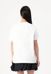 T-shirt en coton blanc avec une coupe décontractée, des manches courtes et un col rond. Le dos présente une texture lisse et un design épuré.