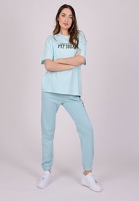 Camiseta de algodón azul claro con un estampado gráfico, combinada con pantalones jogger a juego. Ambos tienen un corte relajado y puños acanalados. Zapatillas blancas.