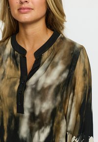 Brun og sort tie-dye skjorte med en stolpe, knapspecifikationer og en blød, gennemsigtig tekstur. Designet har lyse og mørke svunget. 