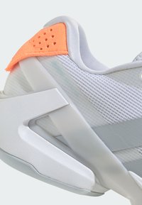 Bílé sportovní boty s texturovaným síťovaným svrškem, se světlým oranžovým semilorem na patě a bílou podpůrnou podrážkou.