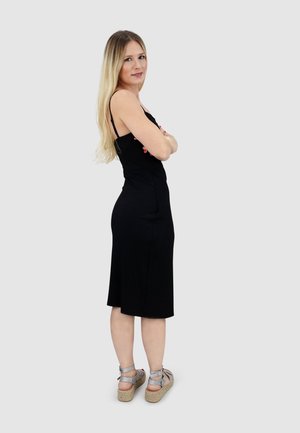 Black ribbed midi dress with thin straps, fitted design, flaring slightly at the hem. Paired with silver strappy wedge sandals.