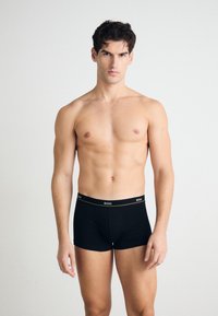 Fekete boxer alsónadrág puha anyagból, kontrasztos fehér és arany díszítéssel ellátott logós derékkal, testhezálló kialakítással.