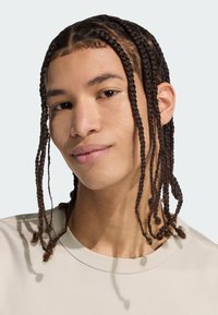 Zapletený účes s dlhými hnedými prameňmi. Obsahuje svetlobežový crewneck sveter a jemnú textúru pleti. Neutrálne pozadie.