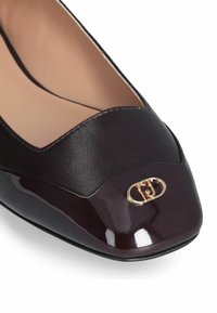 Balerini din piele burgundă închisă cu vârful din piele întinsă lucioasă. Prezintă un accent cu logo auriu și un design cu profil scăzut. Textură netedă.