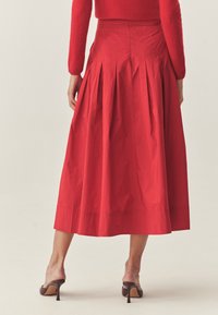 Rote plissierte Midi-Rock aus leichtem Stoff, mit hohem Bund und glatter Textur. Der Saum reicht unter das Knie.