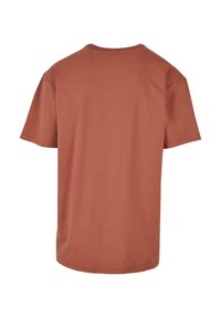 Tricou din bumbac de culoare ruginită, cu mâneci scurte, guler rotund și tiv drept. Textură netedă, fără modele sau grafice.