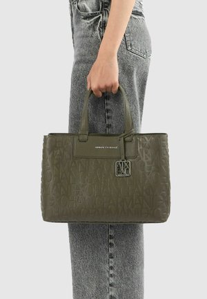 Personne tenant un sac cabas vert olive Armani Exchange avec motif logo embossé, associé à un jean gris en denim.