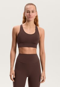 Rjavi športni modrček z zaobljenim izrezom in širokimi naramnicami, oblikovan v oprijetem slogu. Gladek teksturni videz z minimalnimi šivi.