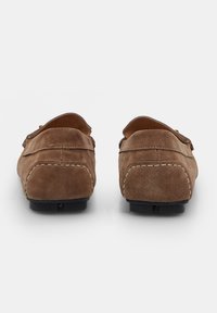 Smeđi suede loafersi s zaobljenim oblikom, s dekorativnim šavovima duž đona i glatkom, teksturiranom površinom.