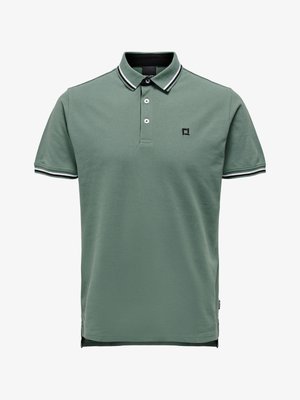 Short-sleeve green polo shirt with black-and-white striped collar and sleeve edges, two buttons, and small black logo on the chest.