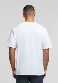 Hvit bomulls T-skjorte med korte ermer, rund hals, avslappet passform, ensfarget design, glatt tekstur, bakfra som viser sømdetaljer.