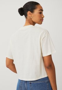 T-shirt court à manches courtes en crème, fabriqué en coton doux. Présente un col rond classique et une coupe décontractée.