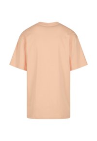 T-shirt de couleur pêche avec un col rond, des manches courtes et une coupe décontractée. Texture lisse, design uni, sans motifs ni accents visibles.