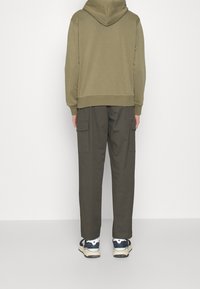 Olivgrön huvtröja med ribbad nederkant, i kombination med mörka cargobyxor med sidofickor och vita sneakers med blå detaljer.