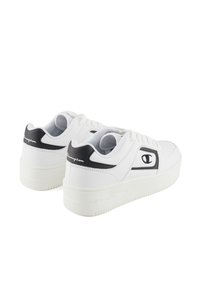 White sneakers with black accents, made of synthetic material, featuring a thick sole, perforated side detailing, and logo on the heel.