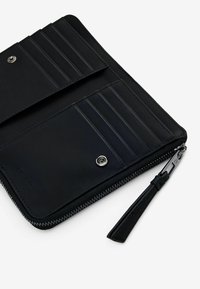 Cartera de cuero negra con múltiples ranuras para tarjetas, cierre con cremallera y detalles de hardware en plata. Textura suave, diseño minimalista y correa para la muñeca.