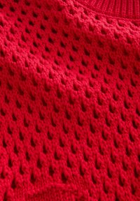 Zbliżenie na czerwoną dzianinę z teksturowanym wzorem małych, równomiernie rozmieszczonych diamentowych otworów.