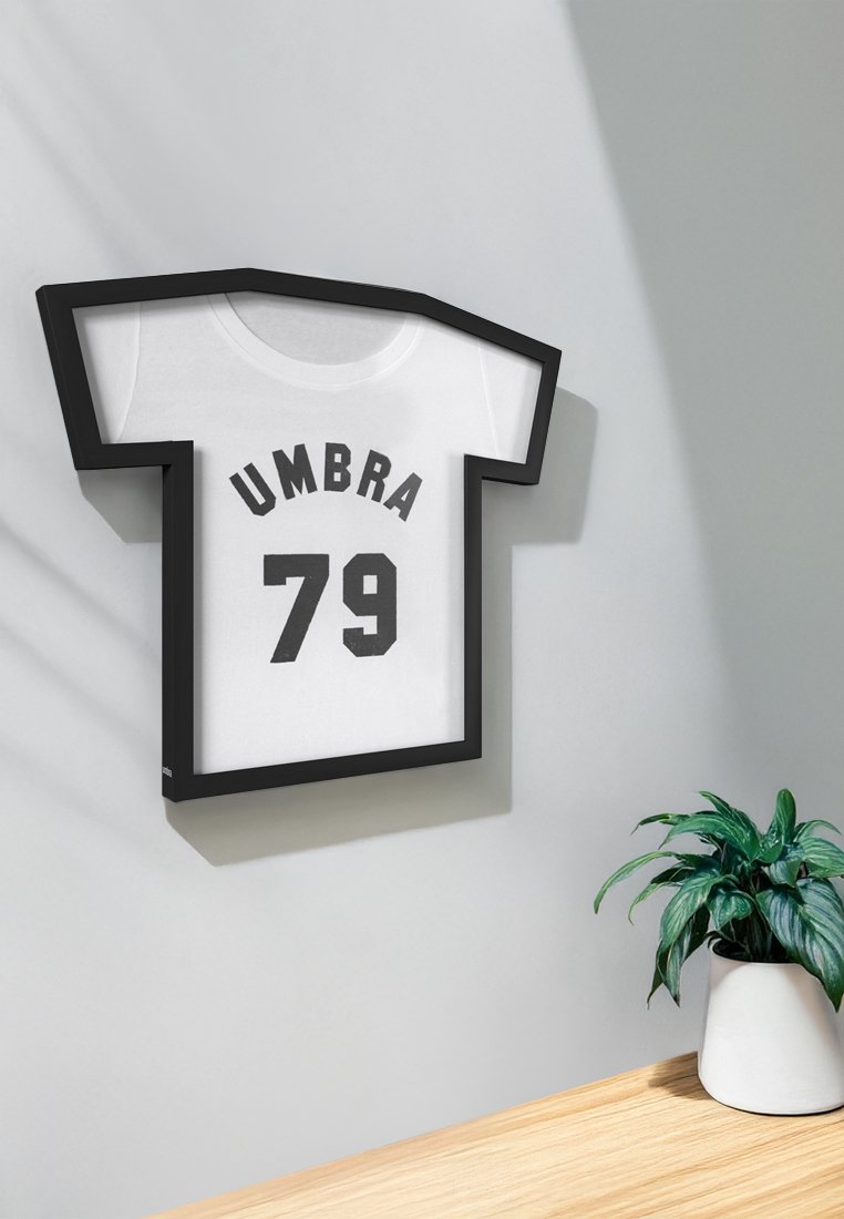 Schattenboxrahmen in Form eines Trikots, schwarzer Rahmen, weißes Trikot mit "UMBRA" und "79" in fetten schwarzen Buchstaben. Materialien aus Holz und Acryl.