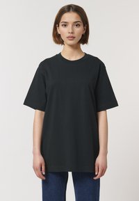 T-shirt en coton noir à manches courtes, col rond et coupe décontractée, associé à un jean en denim bleu. Design simple, sans motifs visibles.