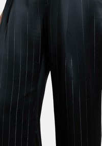 Zwarte broek met een gladde, glanzende textuur, voorzien van verticale streepjes in een licht reflecterend materiaal, met een getailleerde pasvorm.