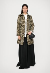 Palton cu model de leopard, având guler și închidere cu nasture, asociat cu o fustă maxi neagră și o poșetă clutch neagră. Textura pare moale și netedă.