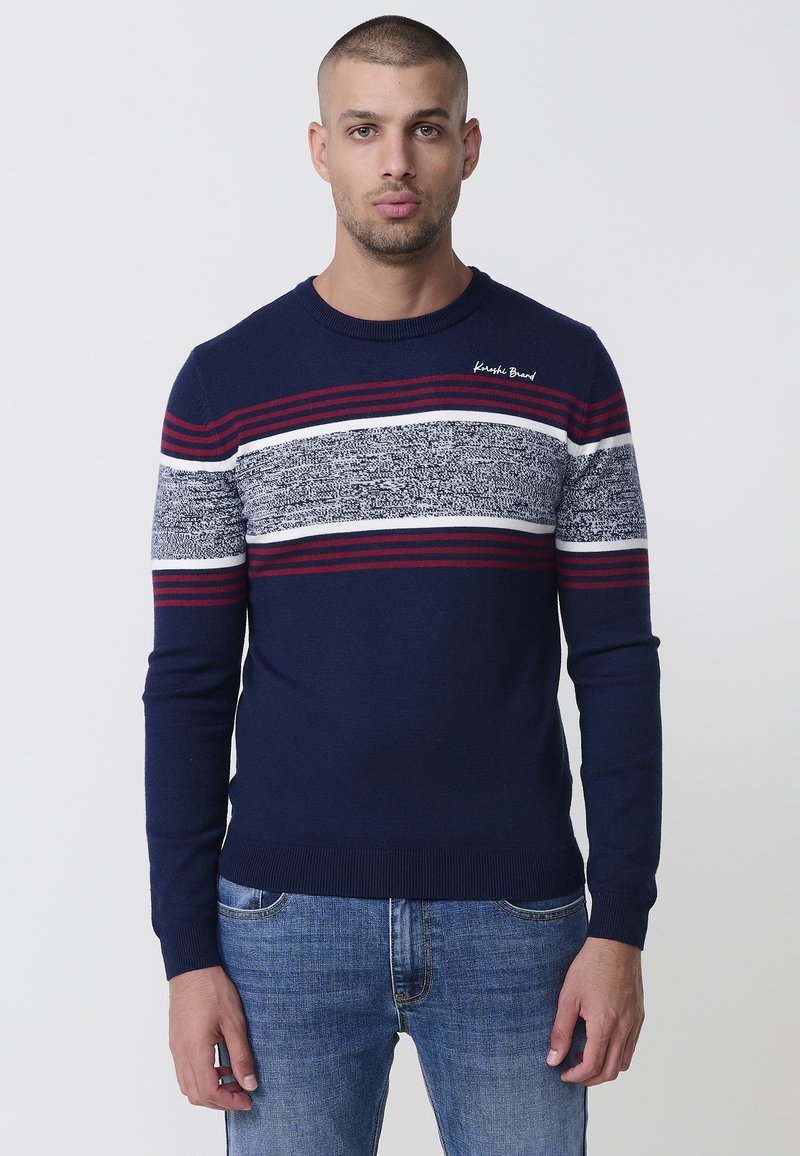 Suéter de punto azul marino con rayas horizontales en rojo, blanco y gris, que presenta un cuello redondo y puños acanalados. El logo está bordado en el pecho.