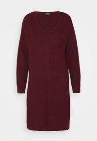 Robe tricotée bordeaux avec un décolleté en V profond, des manches longues et une texture côtelée présentant un motif en chevrons sur le devant. Longueur mi-cuisse.