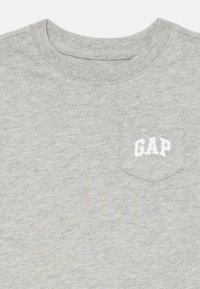 Valkoinen crewneck t-paita, jossa on pieni rintatasku ja valkoinen "GAP"-logo brodeerattuna.