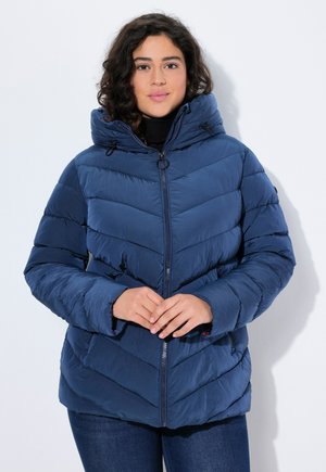 Veste rembourrée bleu marine avec un col haut, motif en chevrons, fermeture éclair à l'avant et capuche avec cordon de serrage. Le tissu semble brillant et lisse.