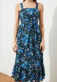 Blumenkleid mit quadratischem Ausschnitt, breiten Trägern, dunkelblauem Hintergrund, lebendigen blauen und mehrfarbigen Blumen sowie einem Volantsaum.